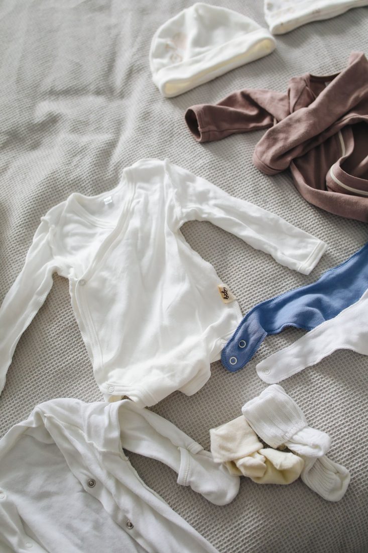 Folded baby clothes and shoes on a soft beige blanket