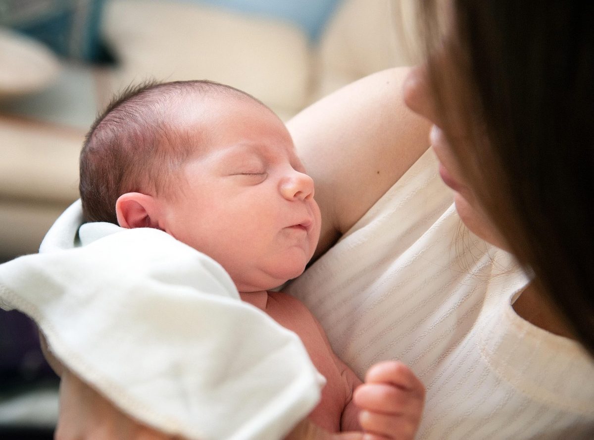 A mother in a cream sweater holding a newborn